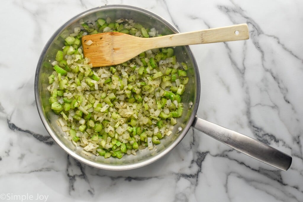 overhead of saucepan of diced onion and celery with a wooden spoon to make Cornbread Stuffing