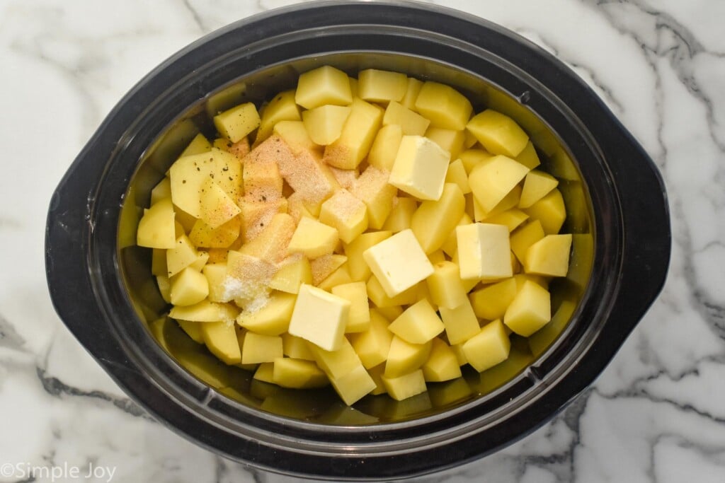 overhead of crockpot of peeled and diced potatoes, butter, and seasonings to make Crockpot Mashed Potatoes