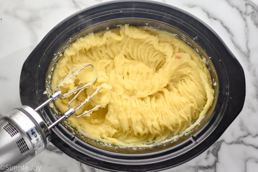 overhead of crockpot of mashed potatoes, handheld mixer sitting beside