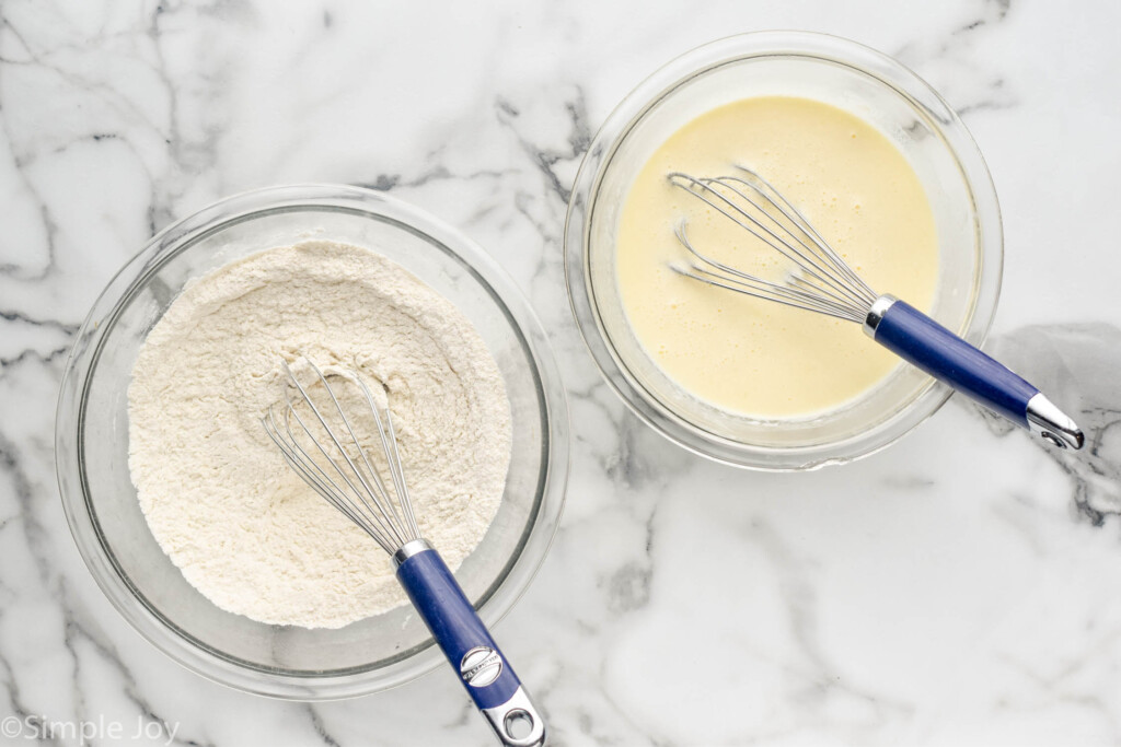 two glass bowls of waffle ingredients with whisks