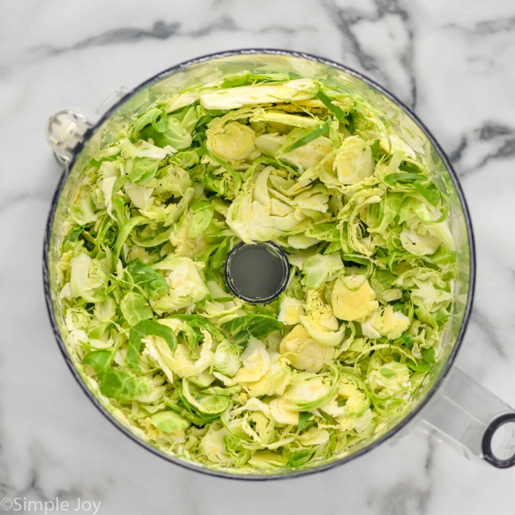 overhead of food processor of shaved brussels sprouts to make Shaved Brussels Sprout Salad