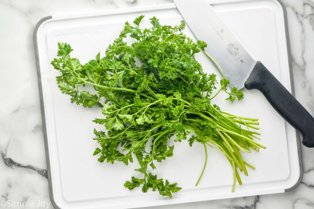 overhead of bunch of fresh parsley on a white cutting board with knife sitting beside to show How to Store Parsley