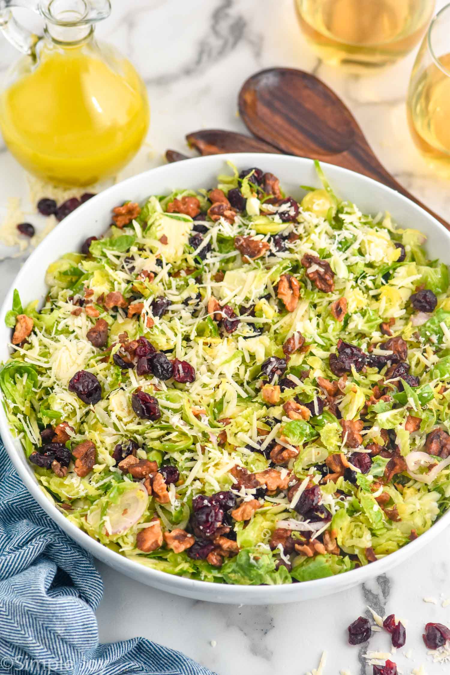 Bowl of Shaved Brussels Sprout Salad topped with shredded parmesan cheese with dressing and spoon for serving sitting in background