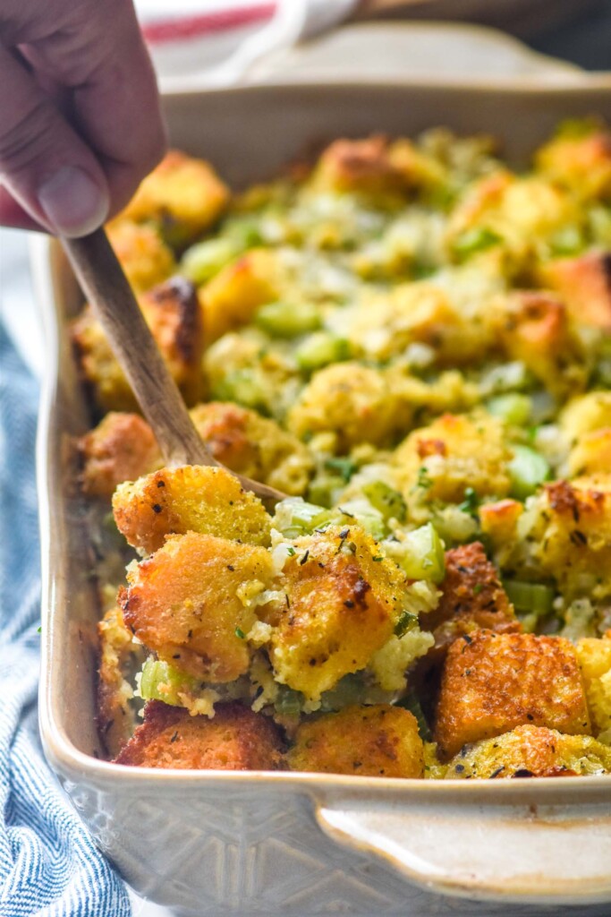 Man's holding holding spoon in baking dish of Cornbread Stuffing