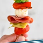 Pinterest graphic for Antipasto Skewers. Image shows person's hand holding Antipasto Skewer. Text says "Antipasto Skewers simplejoy.com"