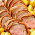 Pinterest graphic for Bacon Wrapped Pork Tenderloin recipe. Text says, "bacon wrapped pork tenderloin simplejoy.com." Image shows platter of sliced Bacon Wrapped Pork Tenderloin and potatoes.