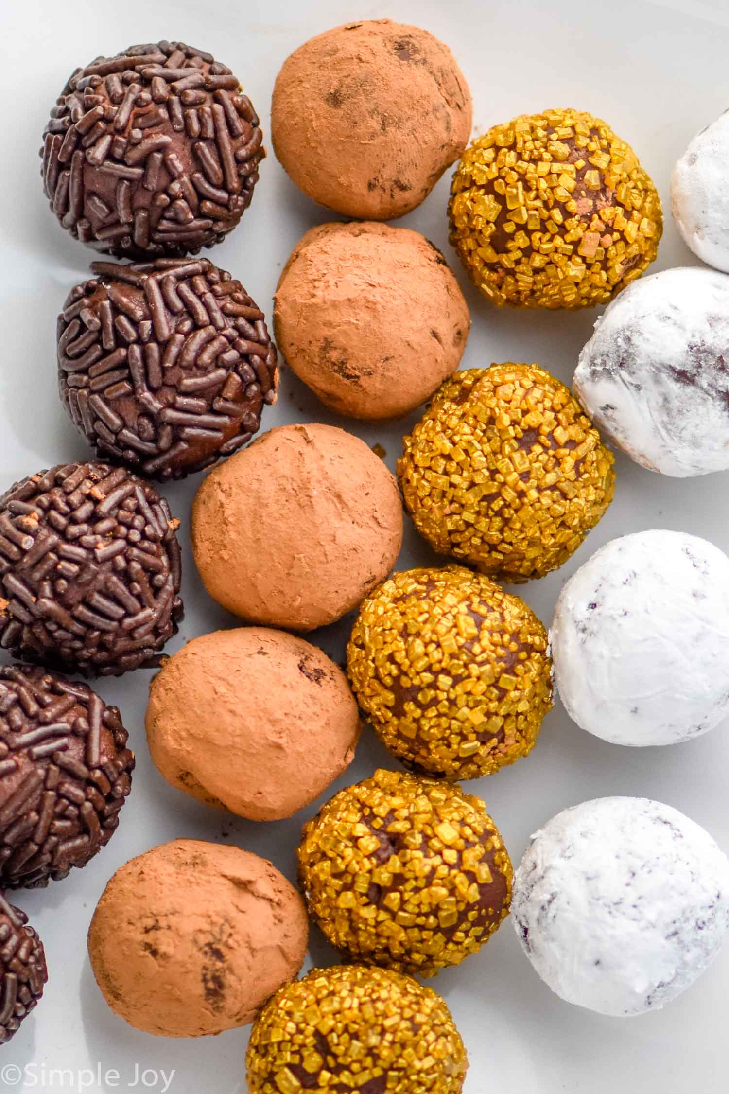 overhead of various chocolate truffles, covered in sprinkles, cocoa powder, gold sprinkles, and powdered sugar