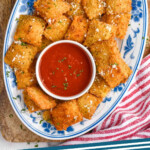 Pinterest graphic for Fried Ravioli. Image shows overhead of a plate of Fried Ravioli topped with grated parmesan cheese with a bowl of marinara sauce in middle. Says "Fried Ravioli simplejoy.com"