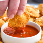 Pinterest graphic for fried ravioli. Text says "the best Fried Ravioli simplejoy.com" Image shows man's hand dipping piece of Fried Ravioli into a bowl of marinara sauce, Fried Ravioli surrounding