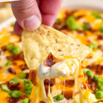 Pinterest graphic for Jalapeño Popper Dip. Says "the best Jalapeño Popper Dip simplejoy.com" Image shows hand holding tortilla chip dipped in Jalapeño Popper Dip topped with diced bacon and green onion