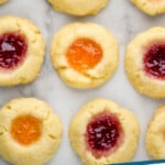 Pinterest graphic for Thumbprint Cookies recipe. Image shows overhead view of Thumbprint Cookies filled with two different colors of jam on the countertop. Text says, "Thumbprint Cookies simplejoy.com."