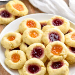 Pinterest graphic for Thumbprint Cookies recipe. Text says, "The best Thumbprint Cookies simplejoy.com." Image shows a plate of Thumbprint Cookies filled with two different colors of jam served on a plate."