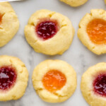 Pinterest graphic for Thumbprint Cookies recipe. Text says, "the best Thumbprint Cookies simplejoy.com." Image is overhead view of Thumbprint Cookies filled with two different colors of jam on countertop.