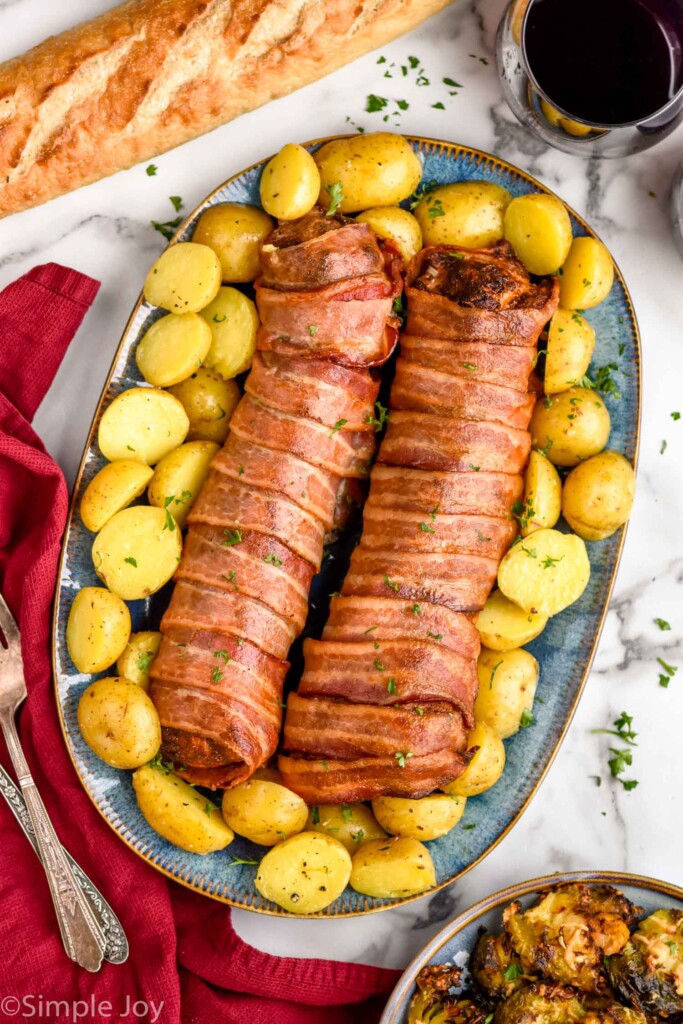 Overhead view of Bacon Wrapped Pork Tenderloin sliced and served on a platter with potatoes