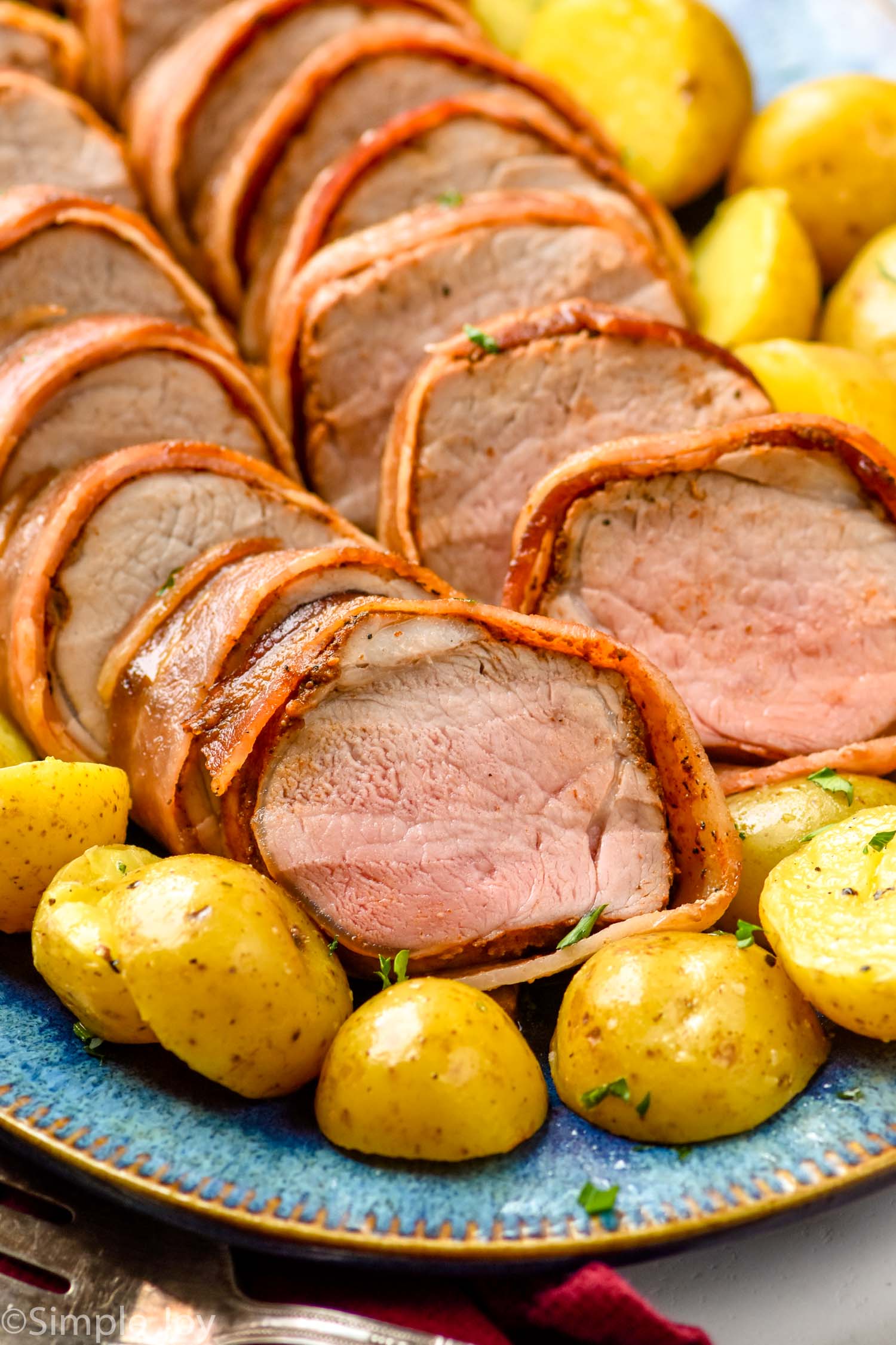 Bacon Wrapped Pork Tenderloin cut and served on a platter with potatoes