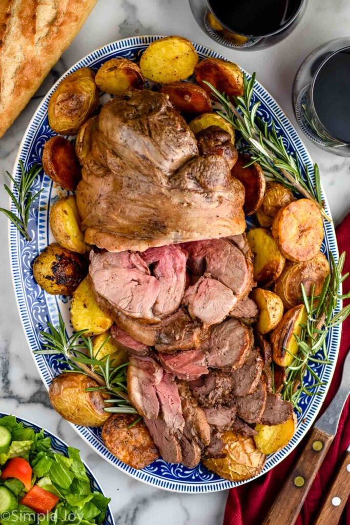 overhead of Boneless Leg of Lamb on a platter surrounded by potatoes and rosemary sprigs