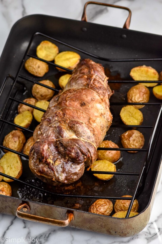 cooked Boneless Leg of Lamb in a roasting pan on a rack with potatoes underneath