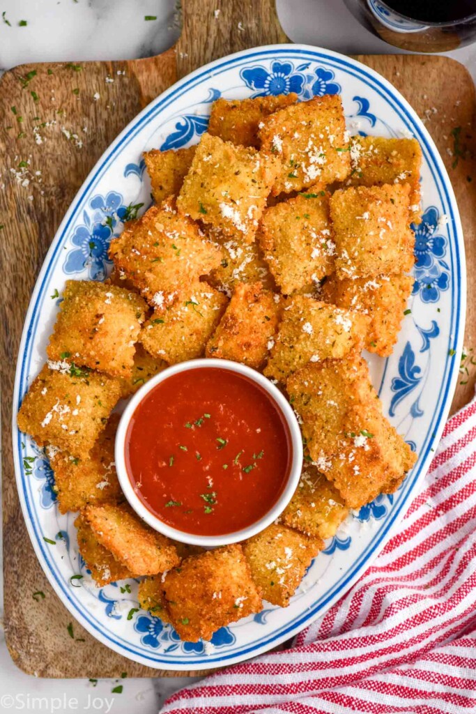 overhead of platter of Fried Ravioli topped with grated parmesan cheese, bowl of marinara sauce sitting in middle.