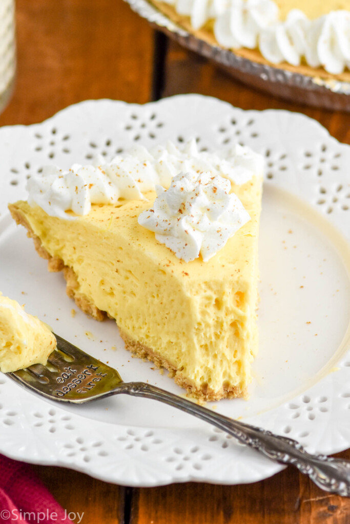 piece of eggnog pie topped with whipped cream with fork and bite of eggnog pie sitting beside on a plate