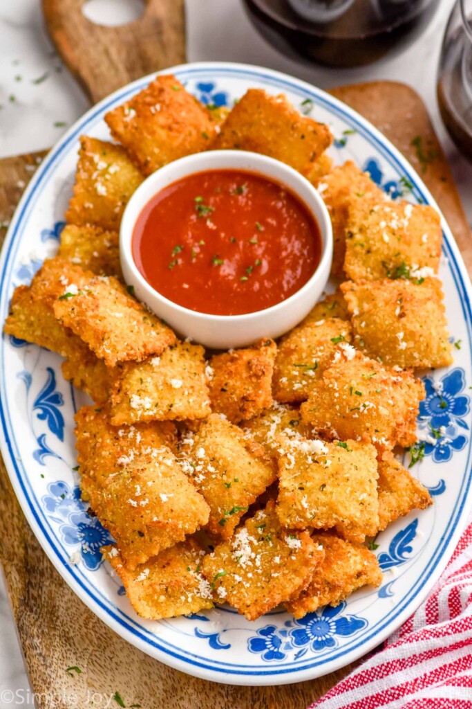 plate of Fried Ravioli topped with grated parmesan cheese with small bowl of marinara sauce sitting in middle.