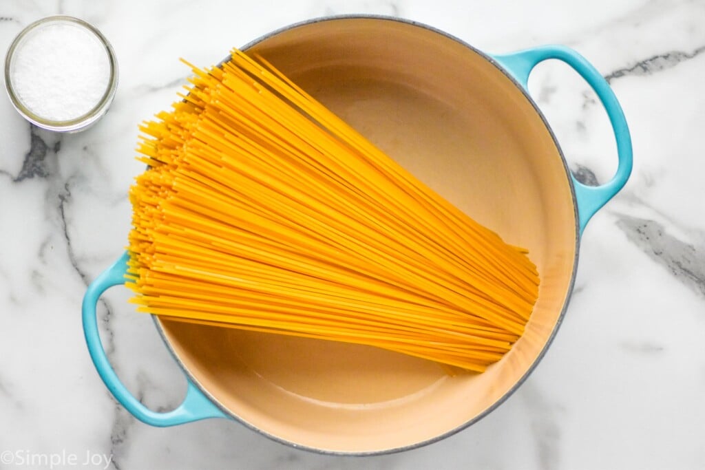 overhead of large pot with dry spaghetti noodles inside with small jar of salt sitting beside to show How to Cook Pasta