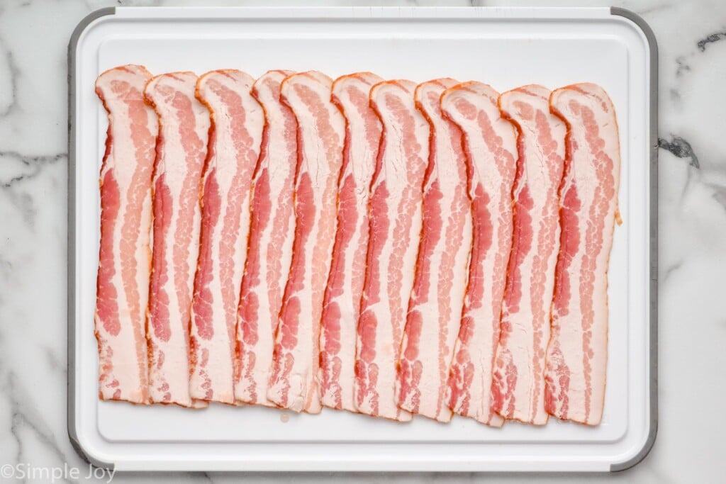 Overhead view of raw bacon on cutting board for Bacon Wrapped Pork Tenderloin recipe.