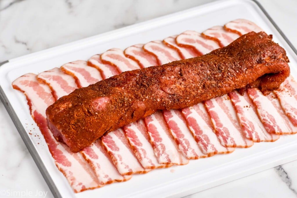 Photo of seasoned pork tenderloin laying on strips of bacon for Bacon Wrapped Pork Tenderloin recipe