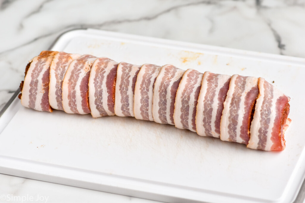 Photo of Bacon Wrapped Pork Tenderloin on cutting board before baking.