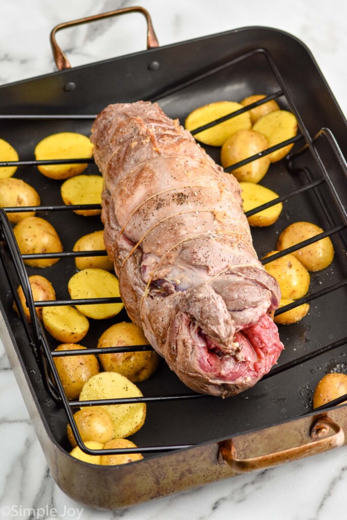 Boneless Leg of Lamb on a roasting pan with wire rack with potatoes underneath