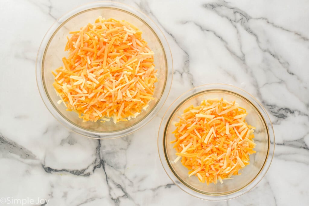 overhead of a large bowl of shredded cheese and a smaller bowl of cheddar cheese, both with a mixture of cheddar cheese and gruyere