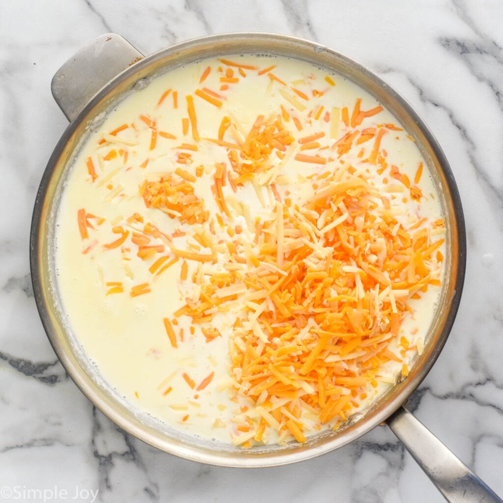 overhead of a skillet with cream sauce and shredded cheese in it