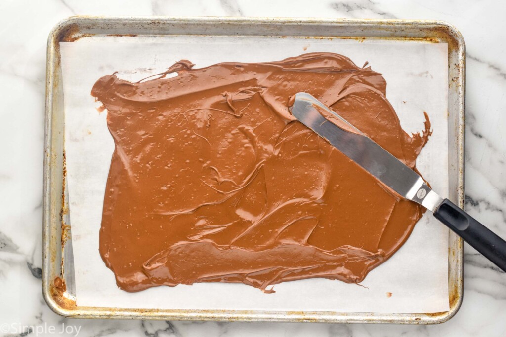 offset spatula spreading out melted chocolate on a parchment lined rimmed baking sheet to make Chocolate Bark