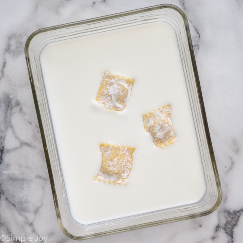 container of buttermilk with three ravioli sitting inside to make Fried Ravioli