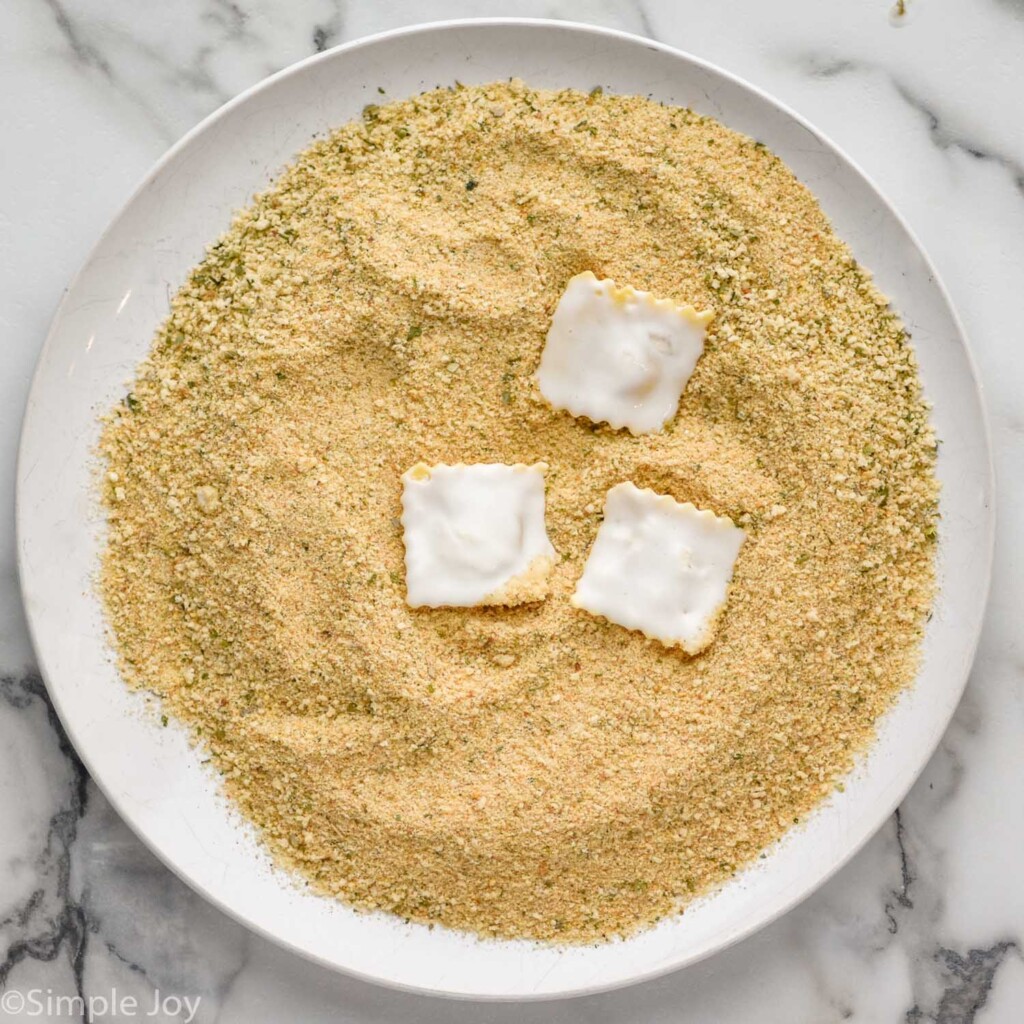 plate of Italian seasoning breadcrumbs with three ravioli on top to make Fried Ravioli