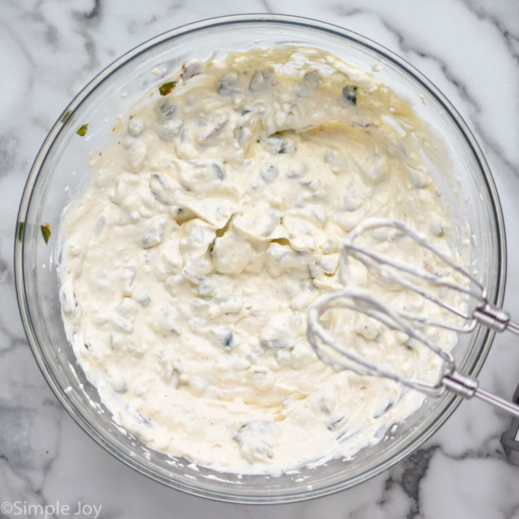 overhead of glass bowl of Jalapeño Popper Dip ingredients with beaters overhead