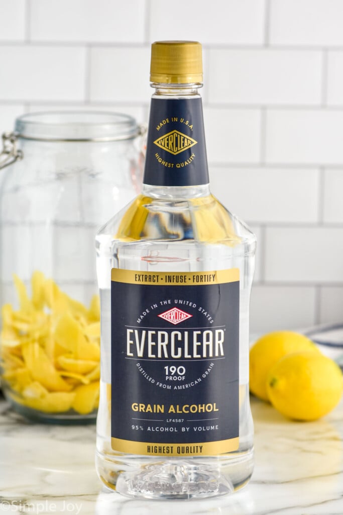 Photo of handle of Everclear alcohol with jar of lemon peels and lemons on counter beside for Limoncello recipe.