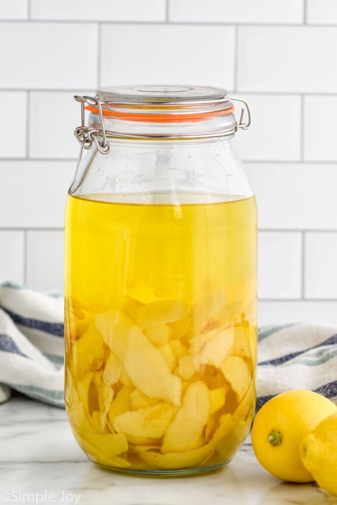 Side view of jar of ingredients for Limoncello recipe. Lemons on counter beside.