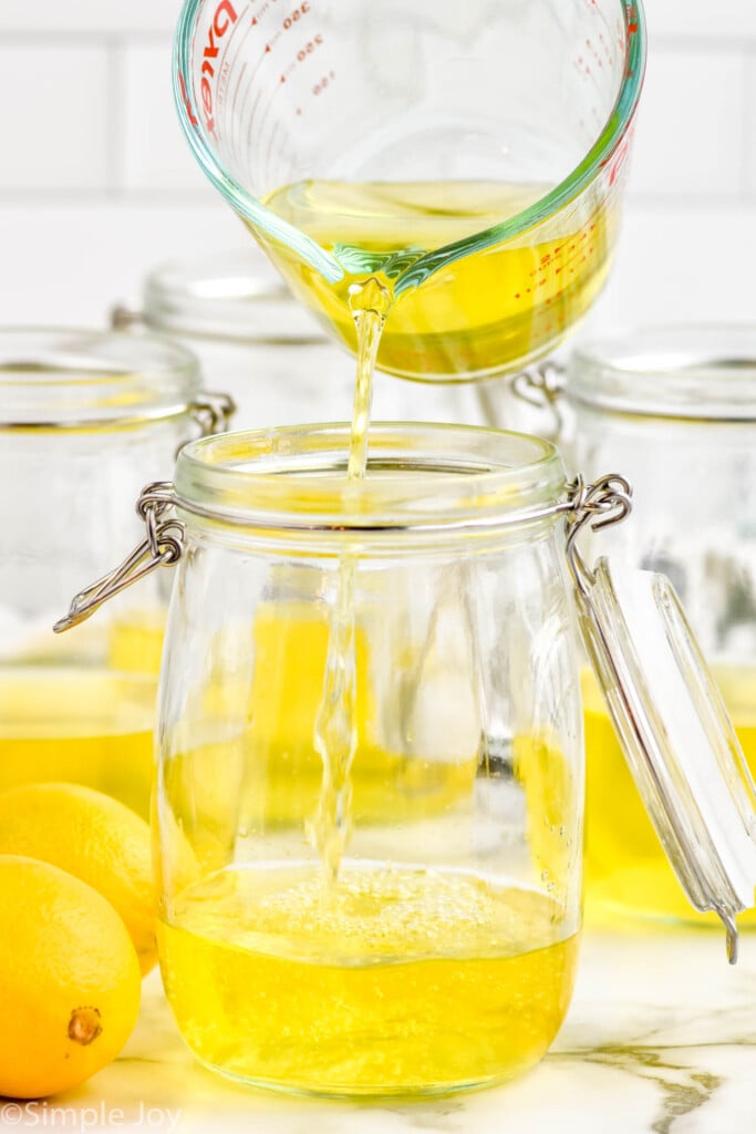 Side view of measuring cup of liquid being poured into a jar of other ingredients for Limoncello recipe. Lemons beside.