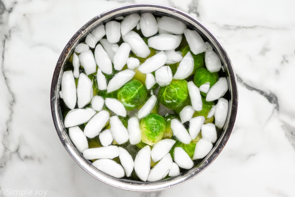 Overhead view of a bowl of ice water with brussels sprouts for Smashed Brussel Sprouts recipe.