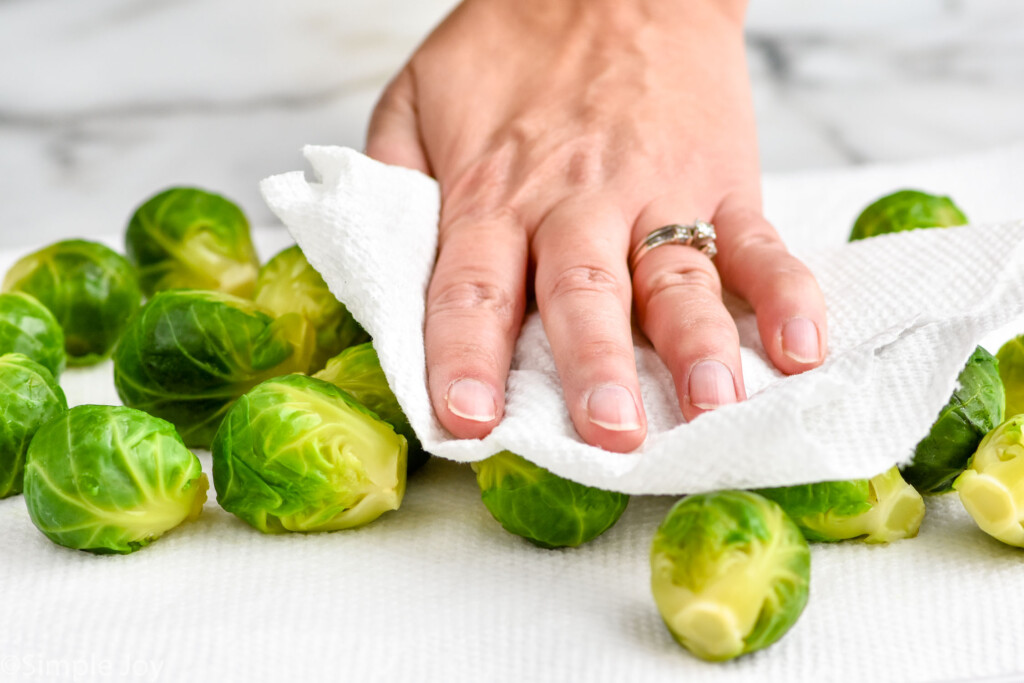 Close up photo of hand with a paper towel drying brussels sprouts for Smashed Brussel Sprouts recipe.