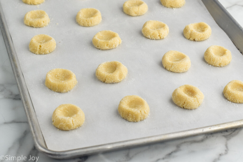 Photo of dough with thumbprints lined up on parchment-lined baking sheet for Thumbprint Cookies recipe.