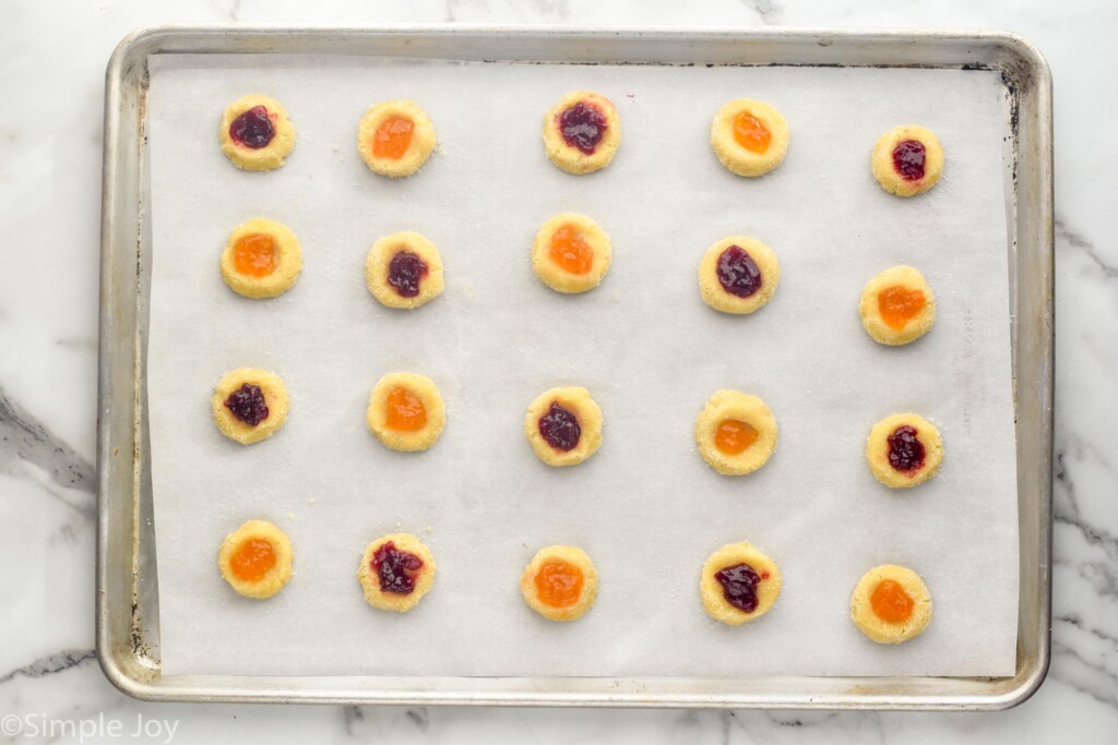 Overhead view of dough with jam on parchment-lined baking sheet before baking for Thumbprint Cookies recipe.