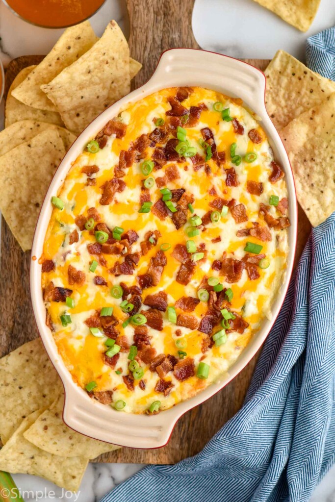 overhead of dish of Jalapeño Popper Dip topped with diced bacon and green onion surrounded by tortilla chips