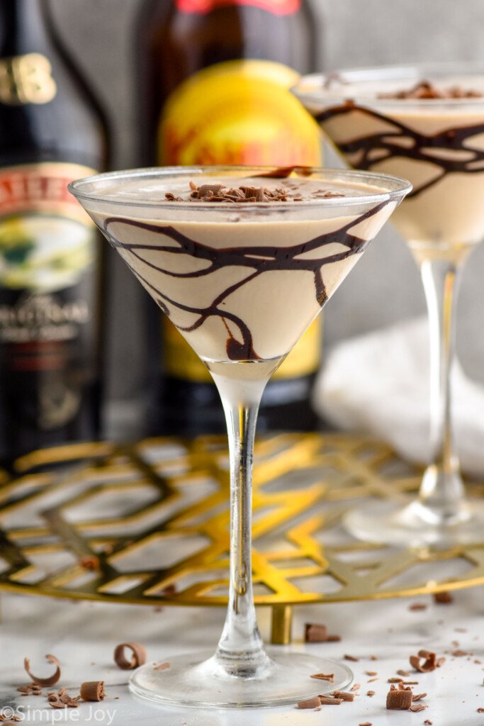 martini glass of Mudslide topped with chocolate shavings. Glass of mudslide, bottle of bailey's irish cream, and bottle of kahlua sitting in background