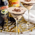 martini glass of Mudslide topped with chocolate shavings. Glass of mudslide, bottle of bailey's irish cream, and bottle of kahlua sitting in background