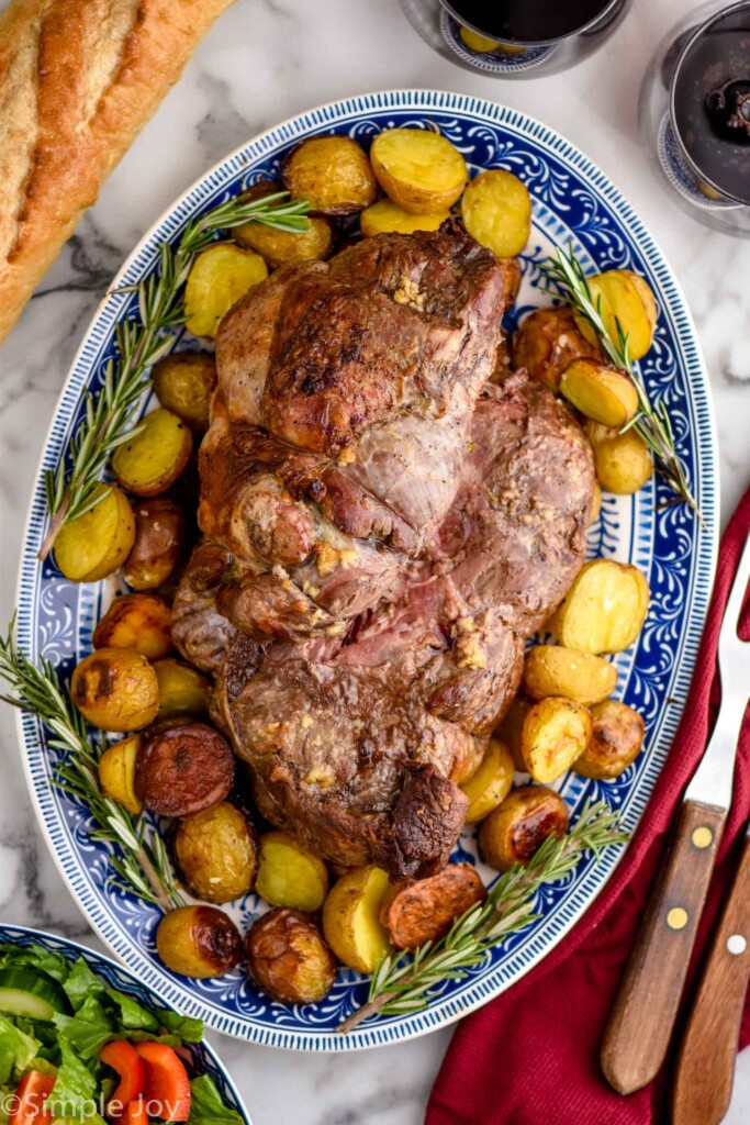 overhead of Boneless Leg of Lamb Recipe on a platter surrounded by potatoes and rosemary sprigs