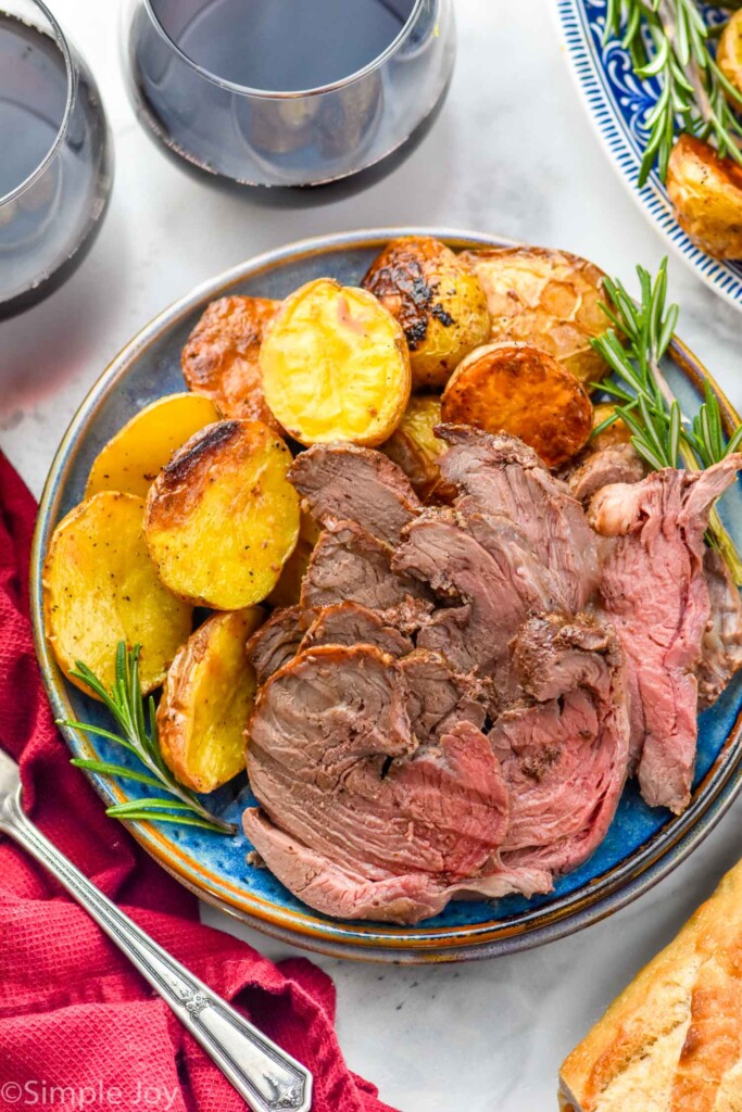 Sliced Boneless Leg of Lamb on a plate with potatoes and rosemary sprig