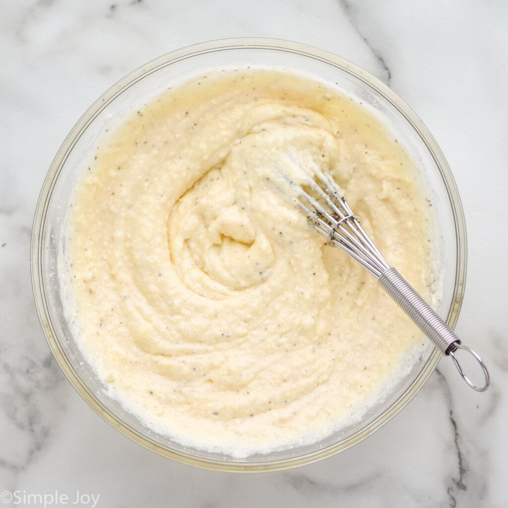 overhead of bowl of Seven Layer Salad dressing with wire whisk.