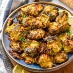 Plate of Smashed Brussel Sprouts with slices of lemon and a loaf of bread beside.