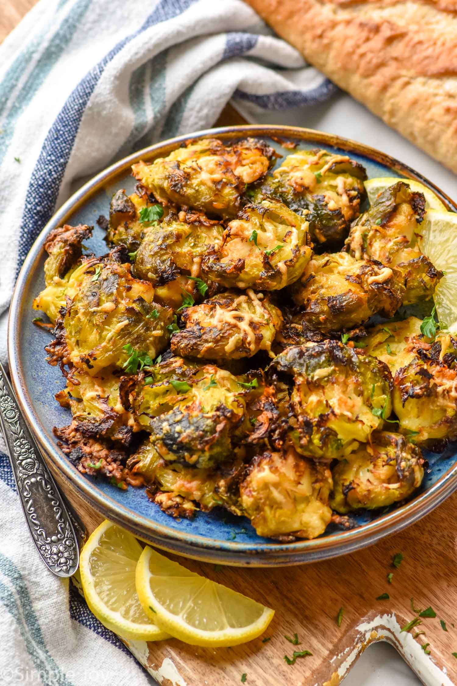 Plate of Smashed Brussel Sprouts with slices of lemon and a loaf of bread beside.